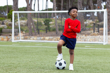 Smiling boy standing on soccer field with ball, enjoying outdoor playtime