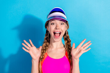Cheerful young woman posing with playful expression in vibrant sportswear against blue background