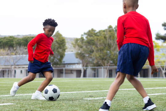 Diverse boys playing soccer on school field, wearing red shirts and blue shorts