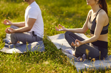 Yogi people couple sitting in lotus pose outdoors on green grass, mudra gesture, meditating, happy calming activity to relax, friends practicing mindfulness in nature, enjoying tranquil setting, peace
