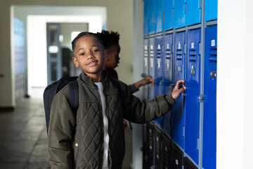 Smiling boy opening locker in school hallway, wearing backpack and jacket
