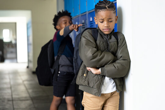 In school hallway, boy feeling sad while another boy teasing him