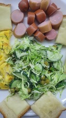 Delicious and appetizing breakfast featuring sliced sausages, crisp salad, omelet, and cheese sandwiches arranged on a plate creating a tasty and satisfying meal .