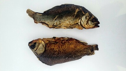 Two dried fish are placed on a white surface, showcasing their golden brown color and slightly weathered texture, a perfect representation of simple, preserved seafood .