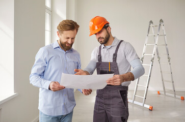 Professional architect in uniform and hardhat, holding house construction blueprint, talking with...