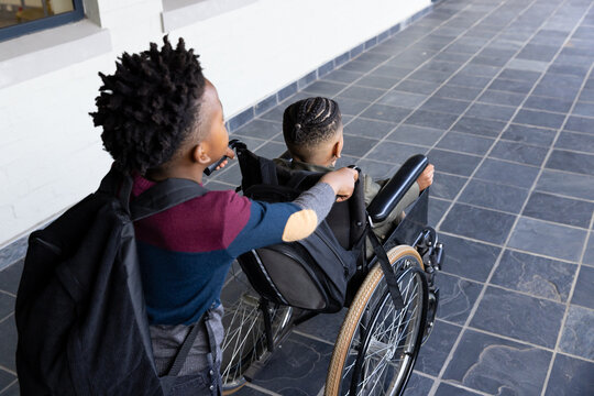 Pushing friend in wheelchair, boy showing friendship and support in school hallway