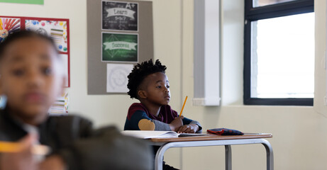 In school, young african american boy attentively listening in classroom, holding pencil at desk