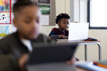 In school, focused african american boy using laptop in classroom, learning with concentration