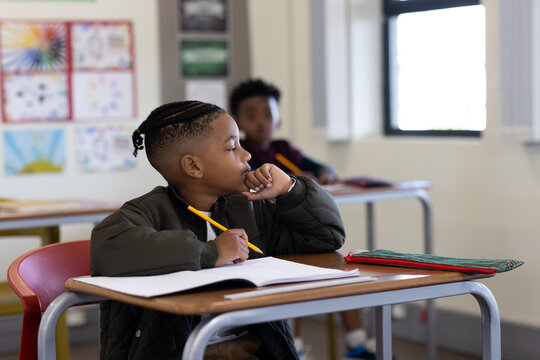 In school, young african american boy thinking with pencil in classroom, looking out window - Powered by Adobe
