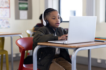 In school, young boy using laptop and headphones, focused on learning