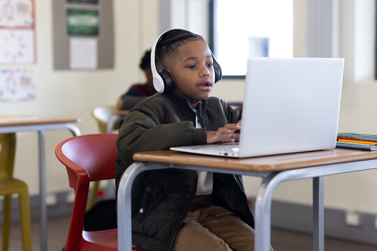 In school, young boy using laptop and headphones, focused on learning