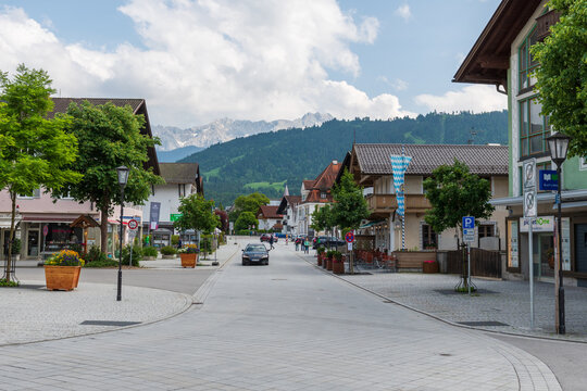 Charming alpine buildings in Mittenwald feature colorful L&uuml;ftlmalerei (frescoes), wooden balconies, and flower-filled window boxes, all set against a dramatic mountain backdrop.