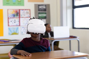 In school, african american boy using VR headset at desk, exploring virtual learning