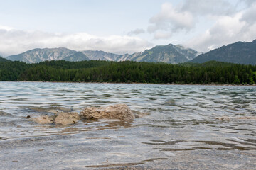 A serene alpine lake with crystal-clear turquoise water mirrors the snow-capped Zugspitze and pine-covered hills. Rowboats glide gently under a clear blue sky—pure alpine tranquility.