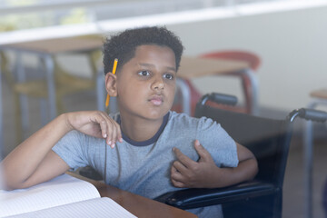 Boy in wheelchair attentively listening in classroom with open notebook, at school