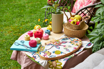 Close-up of a small garden table with embroidery supplies on a warm summer day. Colorful threads,...