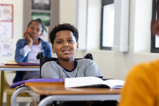 Boy in wheelchair smiling in classroom, engaging with classmates during lesson, at school