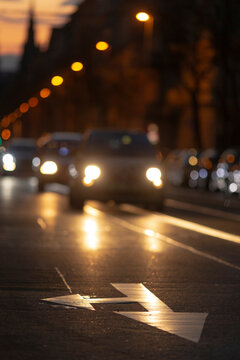 This stunning night photograph vividly depicts a lively city street with oncoming cars and a clear directional arrow, highlighting urban traffic dynamics at dusk, rich in city life