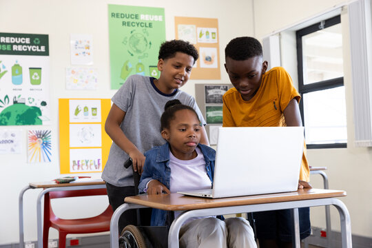 Diverse students collaborating on laptop in classroom, engaged in recycling project, at school
