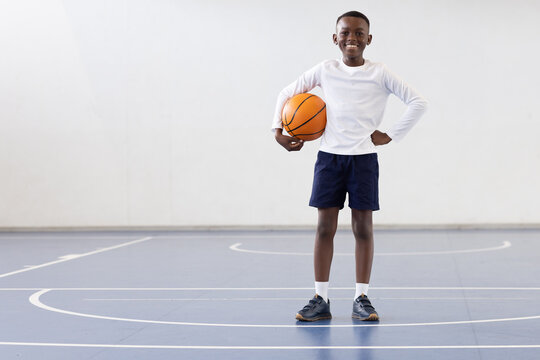 Fototapeta Smiling african american boy holding basketball on court, ready for school sports, copy space