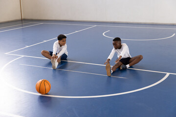 Diverse boys stretching on gym floor with basketball, preparing for school sports activity