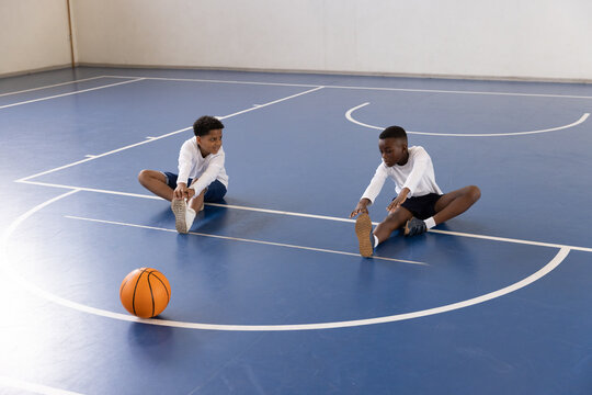 Fototapeta Diverse boys stretching on gym floor with basketball, preparing for school sports activity