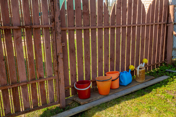 Garden buckets and watering cans in color on the suburban area near the fence