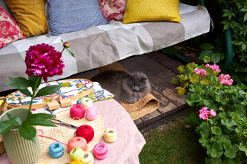 A cozy summer garden scene featuring a cushioned swing used as a relaxing embroidery spot, with a...