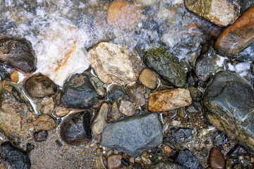 Colorful wet stones in shallow mountain stream
