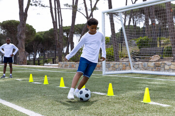 Diverse boys practicing soccer skills on field, dribbling through cones with focus