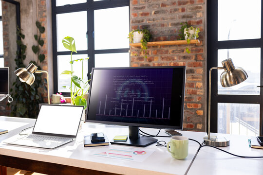 Modern office desk with computer screen displaying coding project and laptop