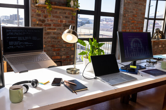 Modern office desk with laptops, coding on screens, and coffee mug