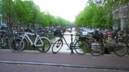 Bicycles lined along an amsterdam canal with trees and buildings blurred in the background, capturing the essence of the netherlands in a soft bokeh style.