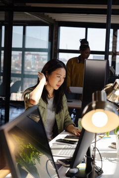 Asian woman coding on computer at modern office, focused and determined