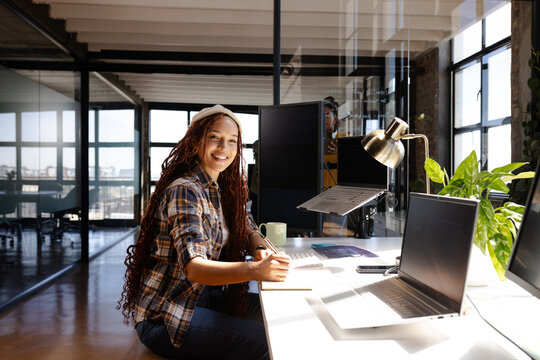 Smiling woman coding at office desk with laptop and coffee mug