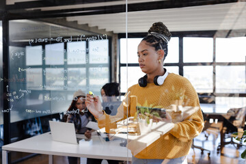 Confident woman writing code on glass board in modern office setting