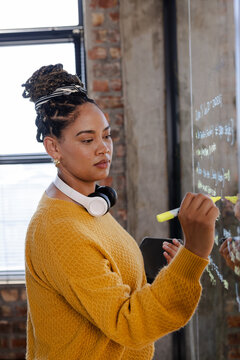 Woman in office writing code on glass board, focused and determined