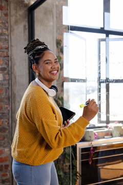 Smiling woman writing code on glass board in modern office environment