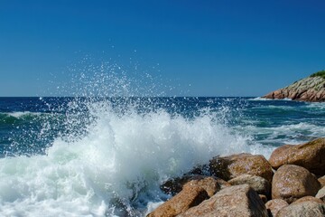 Fototapeta premium Waves crash against rocky shore under a clear blue sky on a tranquil day, Waves crashing on rocky shore under clear blue sky
