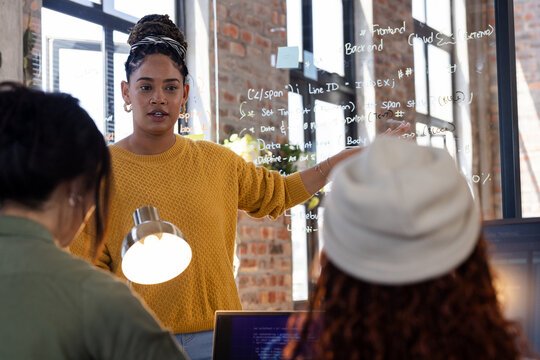 Woman presenting coding ideas on glass board to colleagues in modern office