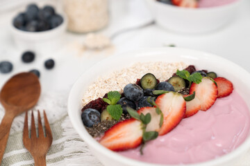 Presented by fruits putting yogurt toppings with strawberry, berry, oats, raisins and chia seed decorated by peppermint in white blow. Pink background. Set of healthy dairy product choice. Pecuniary.