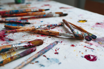 Fototapeta premium Paintbrushes with colorful stains scattered on a table with paint splatters.