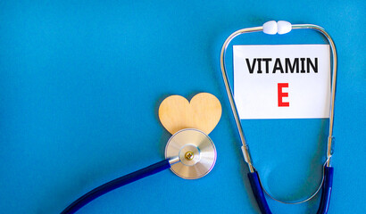 Vitamin E tocopherols symbol. Concept words Vitamin E on beautiful white card. Wooden heart and stethoscope. Beautiful blue background. Medical healthy lifestyle Vitamin E tocopherols concept.