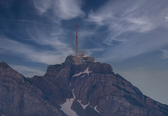 Snow-capped mountain peak with antenna under a dramatic sky at twilight in a remote location