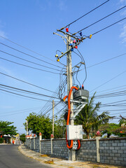 Street power pole with complex electric wiring and colorful connectors against a clear blue sky in...