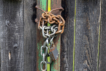 A close-up of a rusty padlock secured with multiple chains on a wooden door. The door features a...