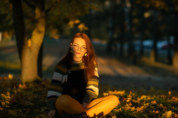 Portrait of a young beautiful red-haired girl in an autumn city park.