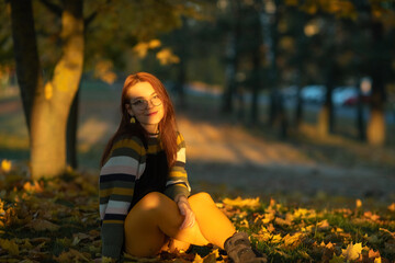 Portrait of a young beautiful red-haired girl in an autumn city park.