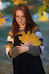 Portrait of a young beautiful red-haired girl in an autumn city park.