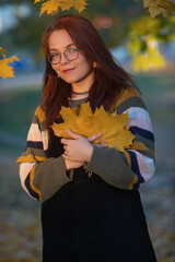 Portrait of a young beautiful red-haired girl in an autumn city park.